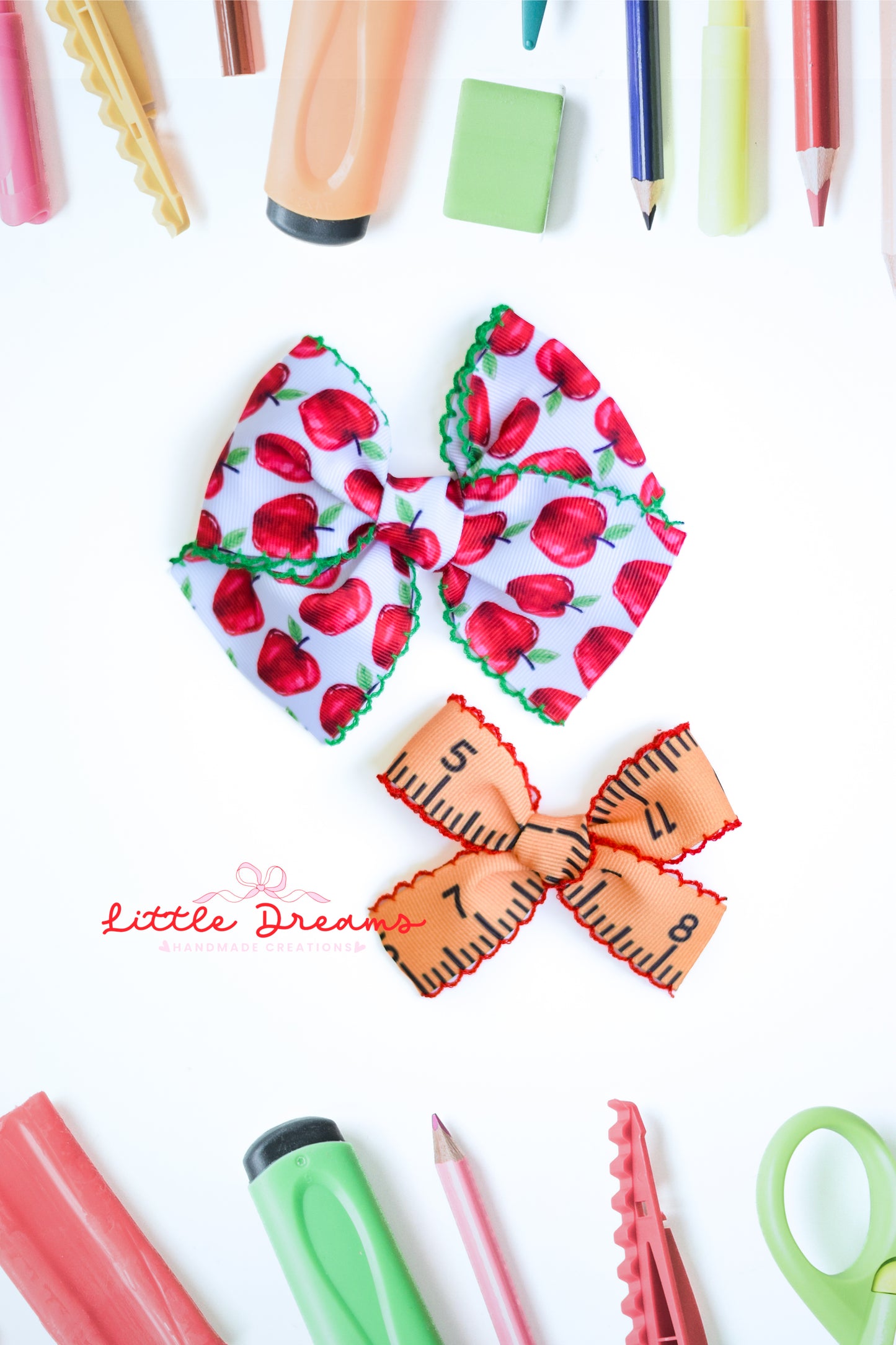 Two ribbon hair bows displayed on a white background, surrounded by school and craft supplies. The bow on the top features a red apple pattern on a white background with green scalloped edges.
The bow on the bottom has a yellow ruler pattern, with black numbers and red scalloped edges.