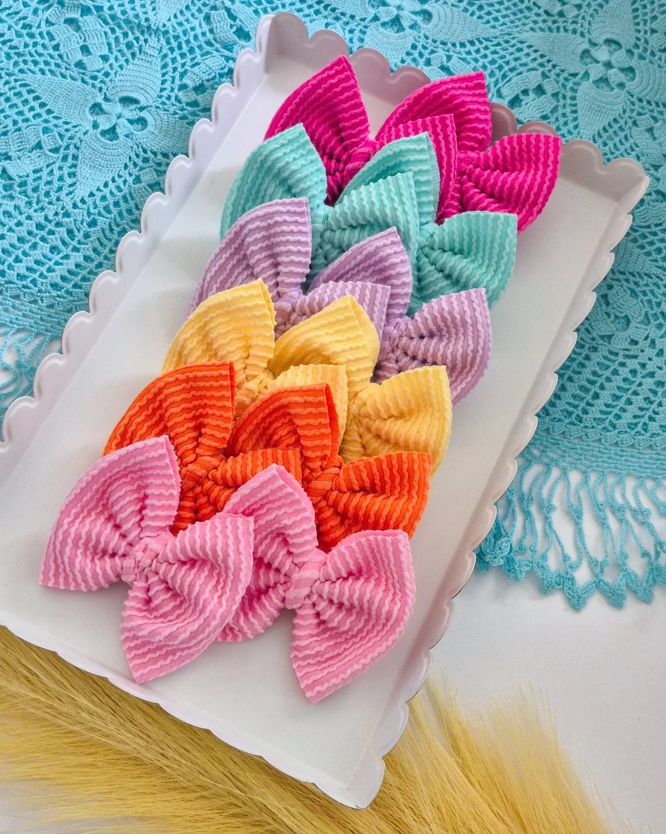 A set of six different small piggies set bows in assorted pastel and bright colors, arranged on a white scalloped tray over a turquoise lace cloth.